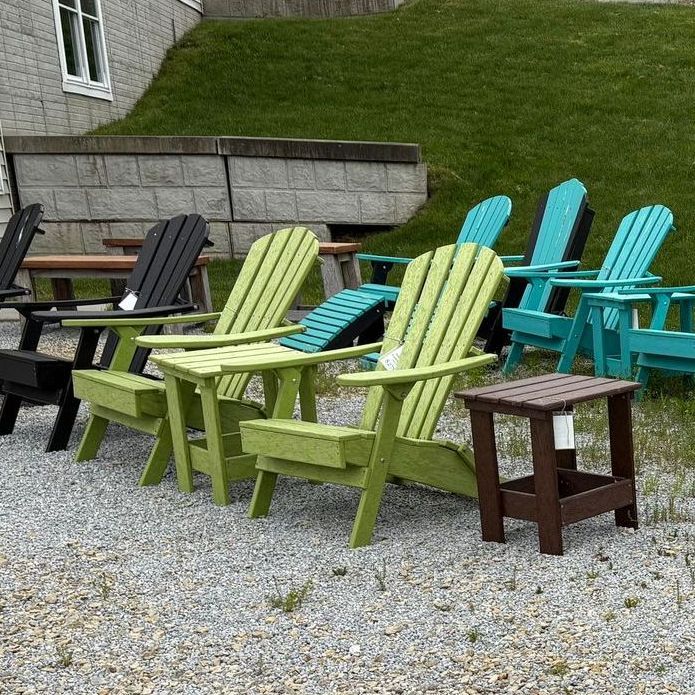 Line of colorful Adirondack chairs and a side table on gravel.