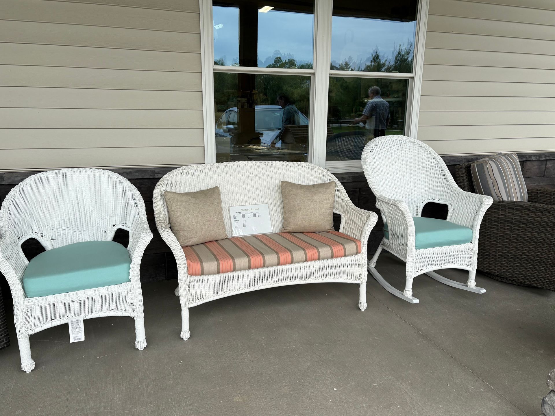 White wicker furniture on a porch: chair, loveseat, and rocking chair with blue and striped cushions.