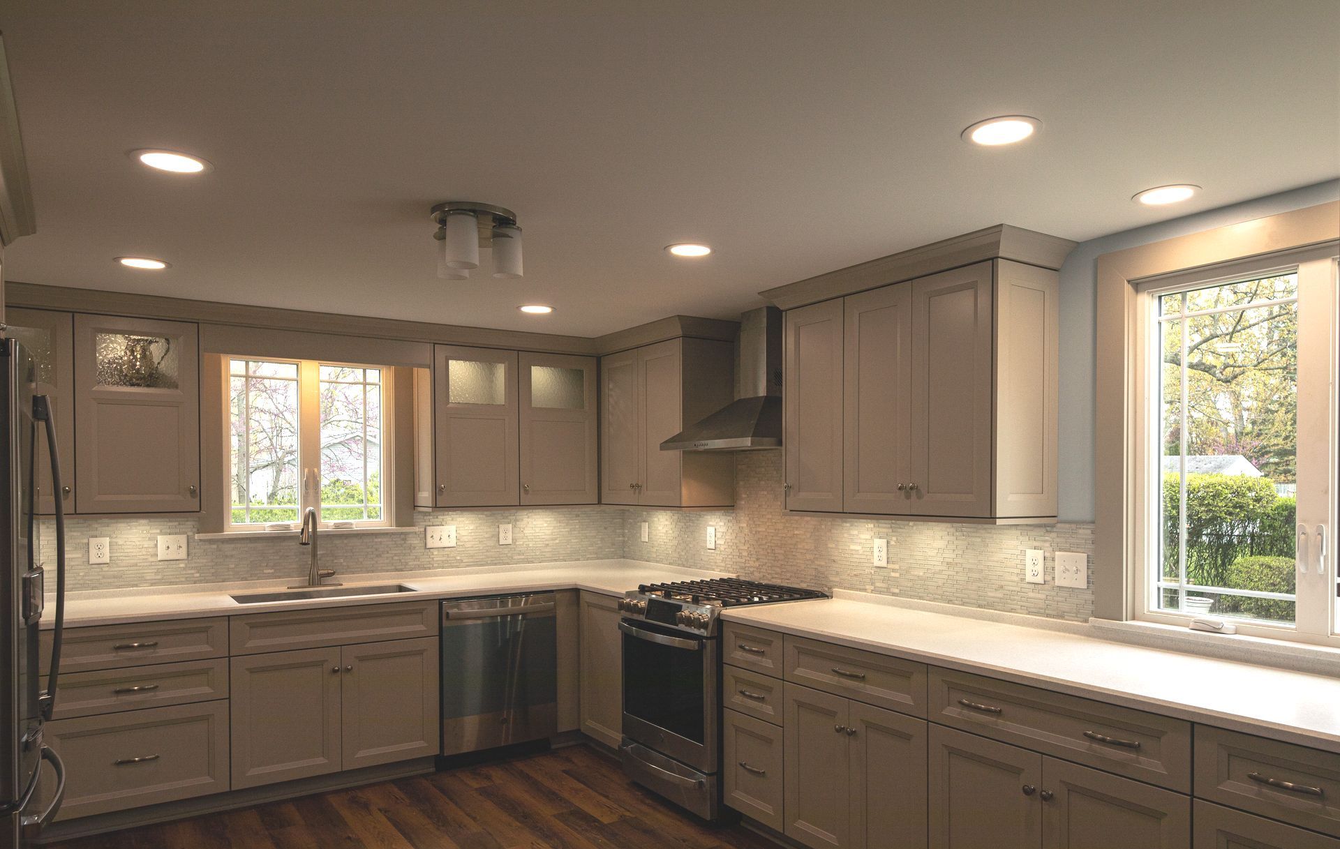 Modern kitchen with beige cabinets, stainless steel appliances, and two windows.