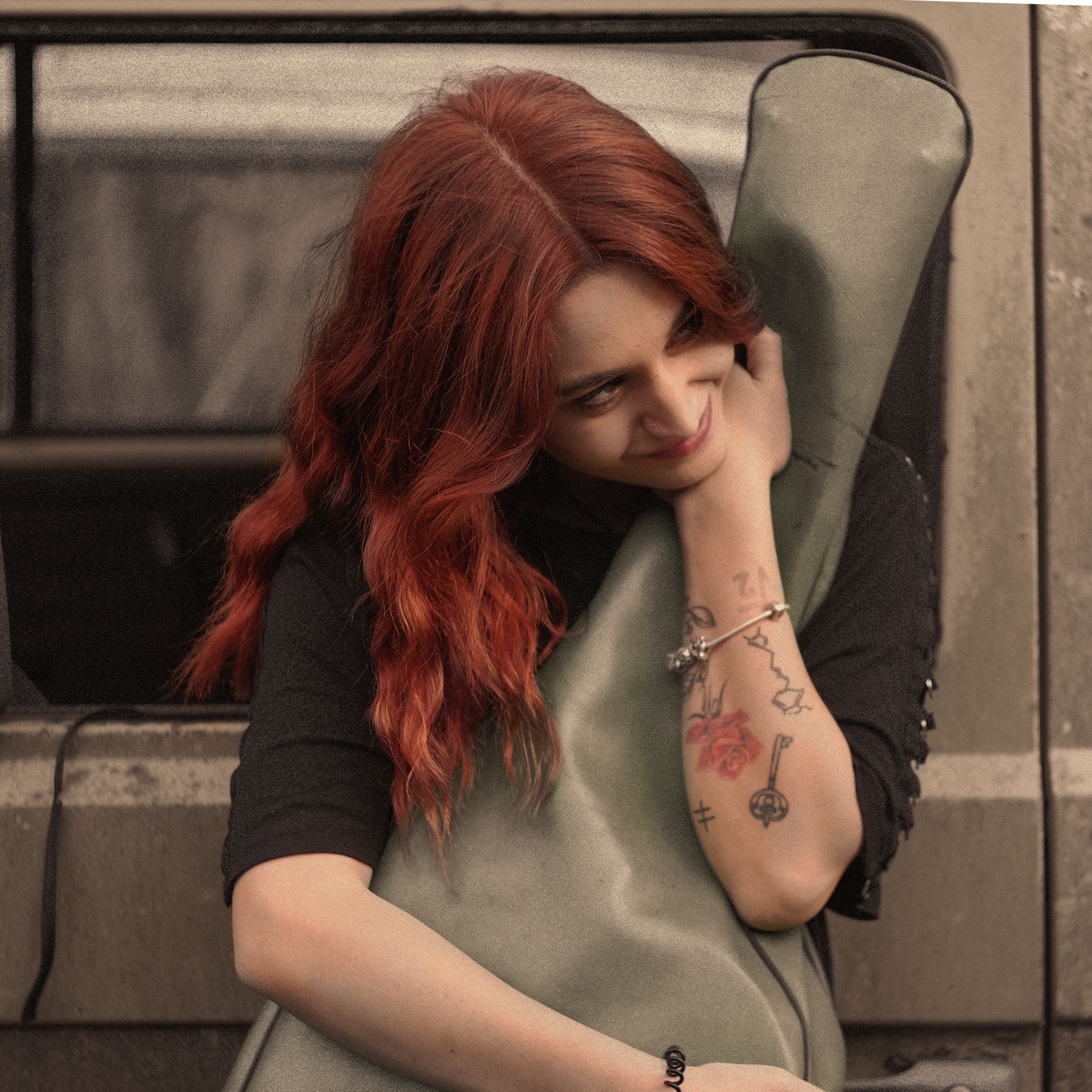 Una persona con i capelli rossicci appoggia la testa contro una custodia verde per strumenti musicali, sorridendo mentre la tiene in mano.
