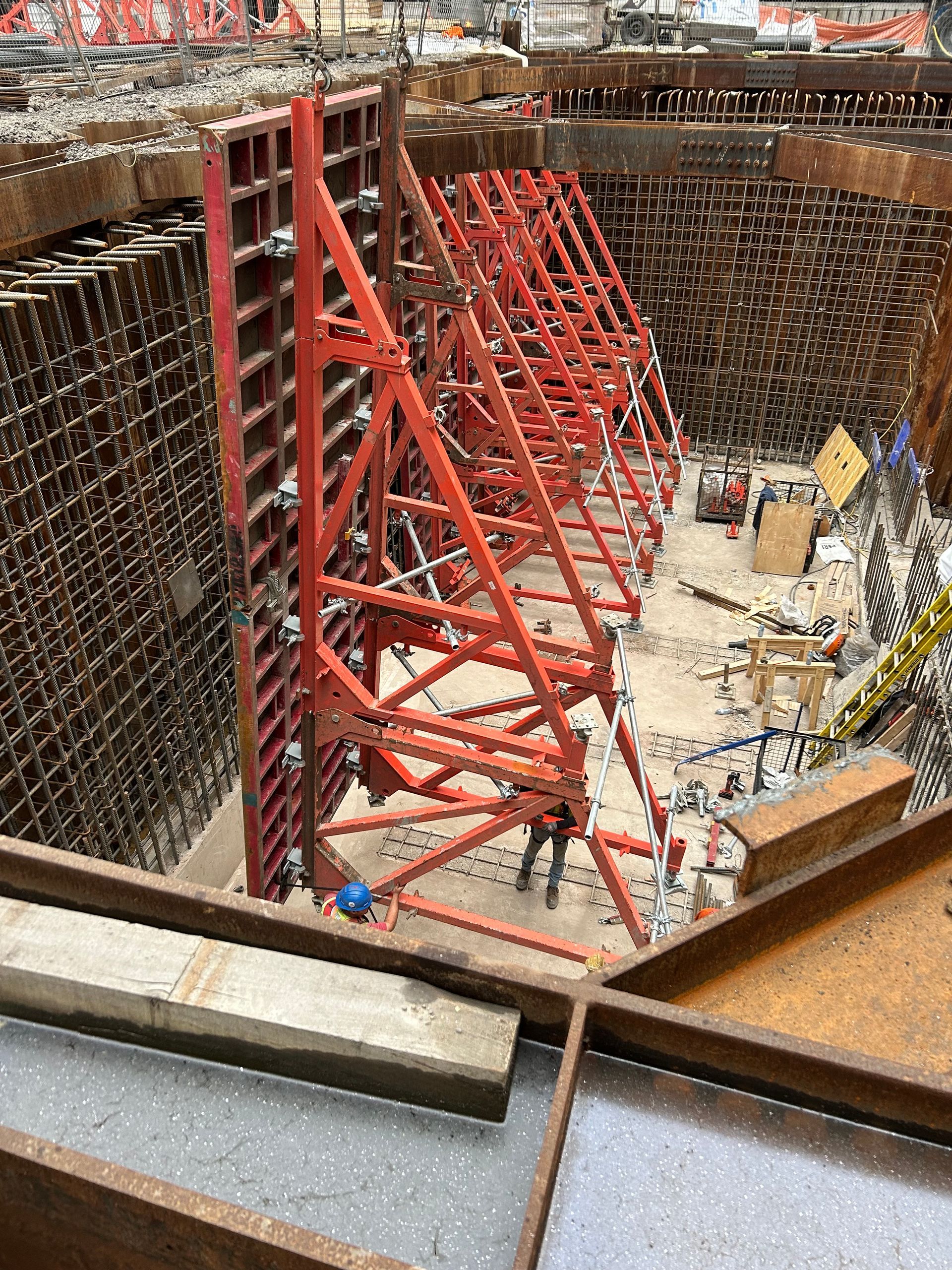 Construction pit with red steel braces and workers inside a deep excavation site.