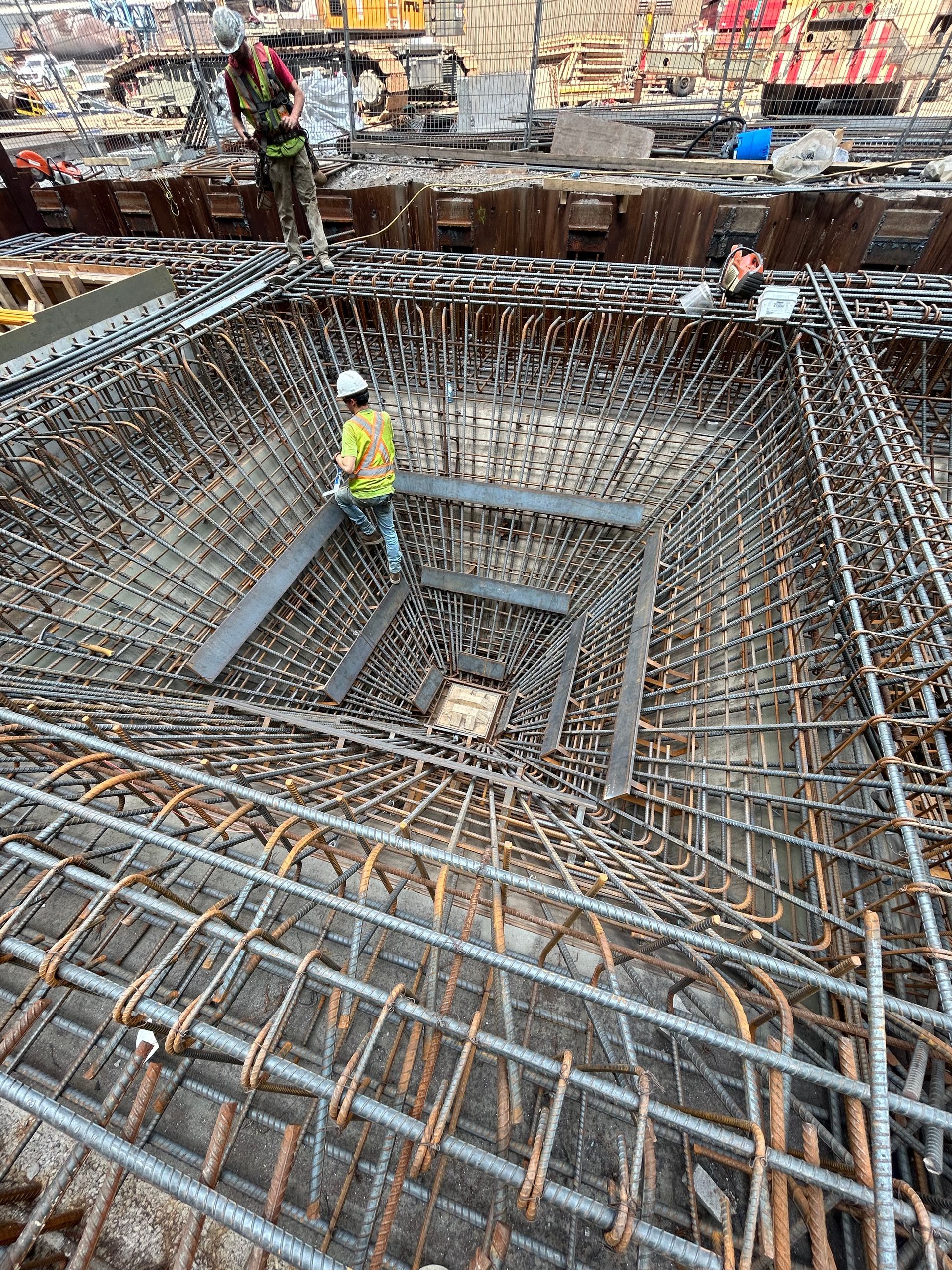 Construction worker in hard hat standing in a deep rebar foundation pit at a building site