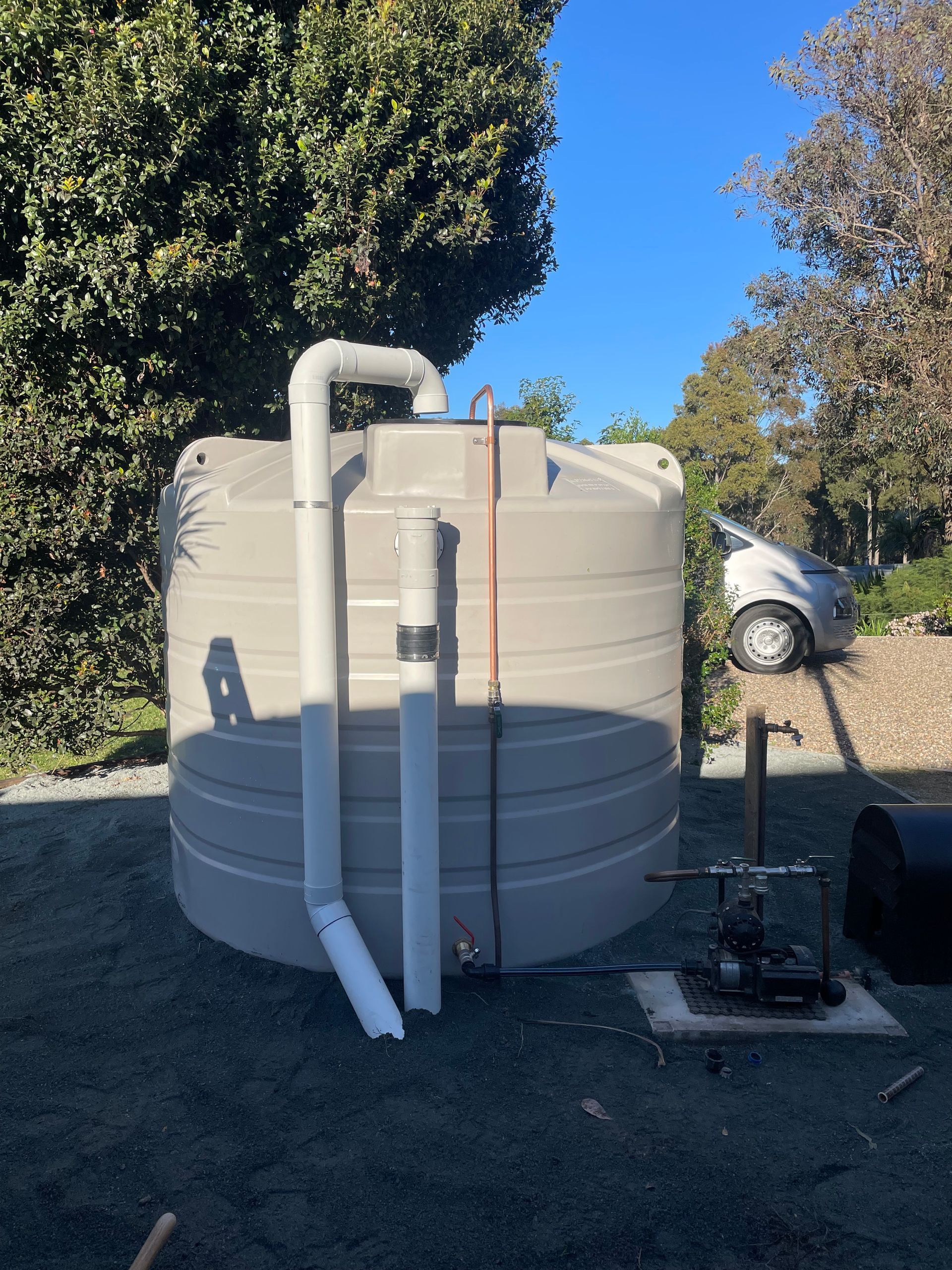 A large water tank with pipes attached to it is sitting in a parking lot.