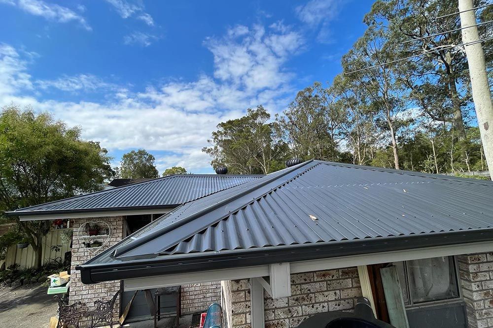 House With Dark Grey Roof And Trees Around It — Roofer in Lake Macquarie, NSW