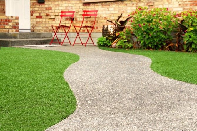 A winding gray stone path leads to a house entrance with two red folding chairs on a small patio next to a green garden.
