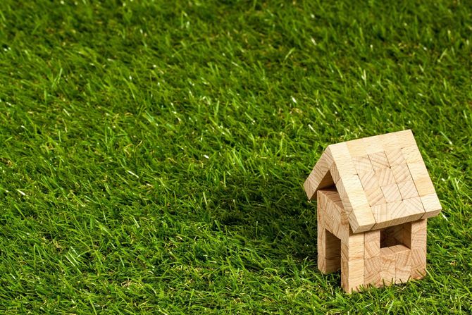 A miniature wooden house model sits on a bright green grassy lawn.