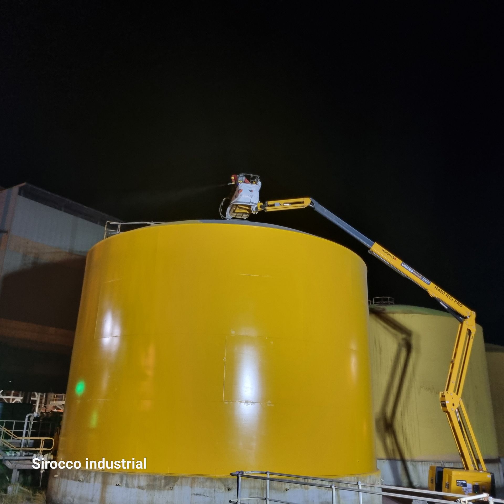 Worker on a lift inspecting the top of a large yellow industrial tank at night — Sirocco Industrial in Pinelands, NT