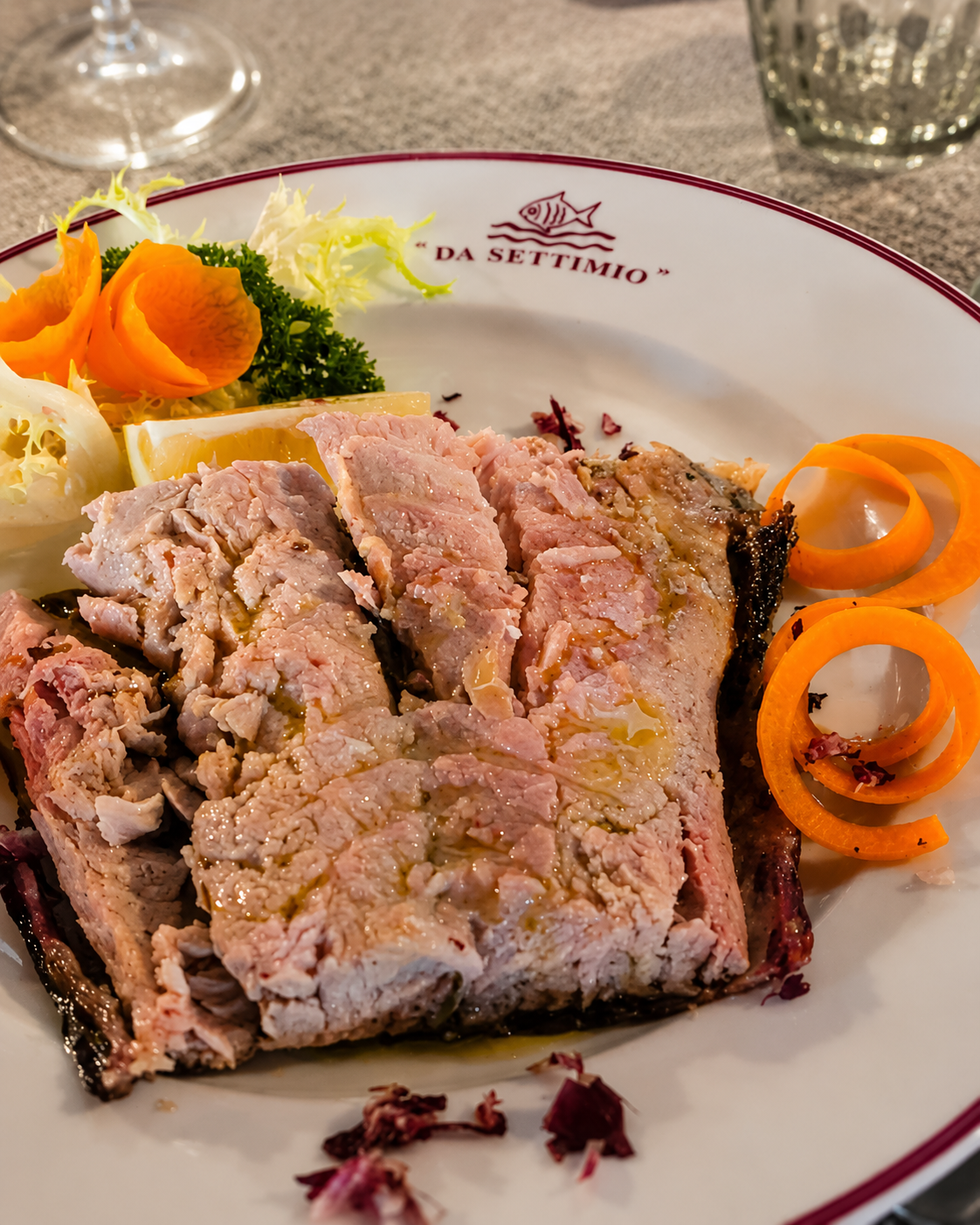Piatto con roast beef a fette, patate arrosto e carote a riccioli su un tavolo di ristorante.