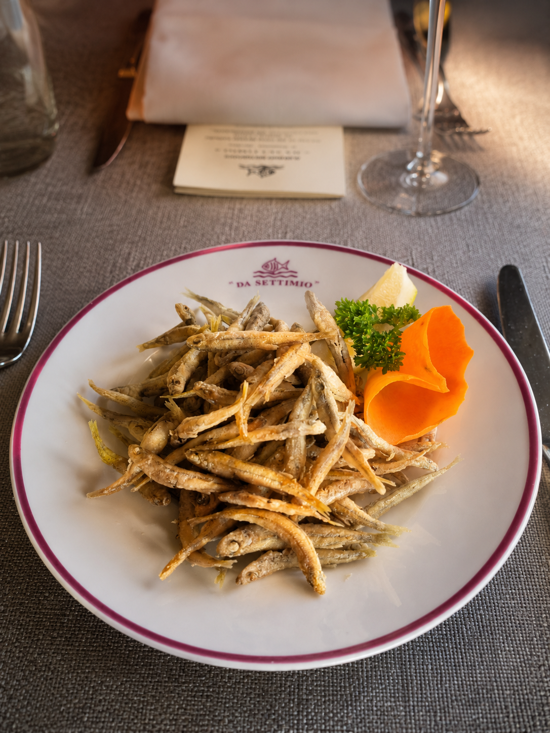 Piatto di bianchetti fritti con prezzemolo e guarnizione d'arancia su un tavolo di ristorante.