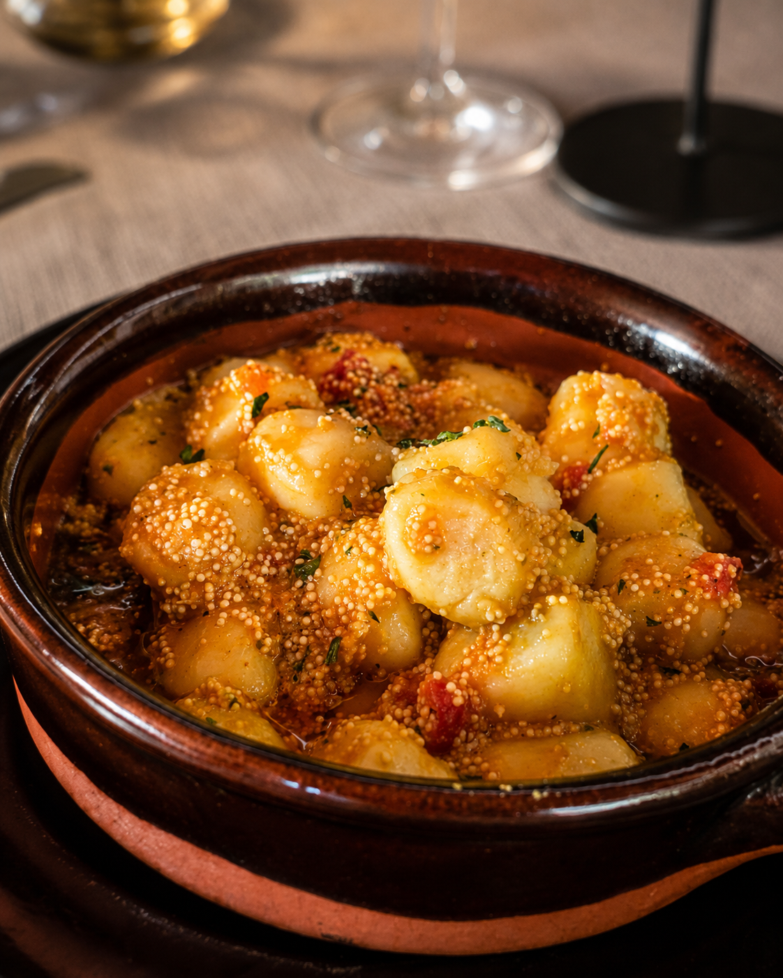 Ciotola di ceramica marrone contenente gnocchi in salsa rossa, guarnita con erbe aromatiche e formaggio grattugiato, su un tavolo.