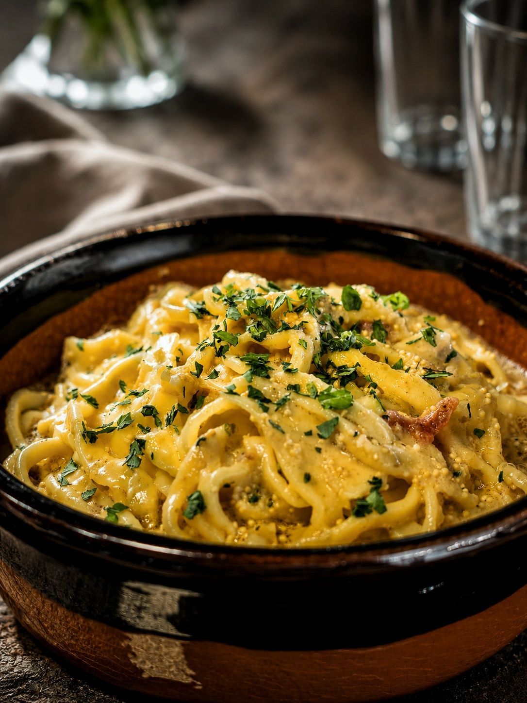 Pasta cremosa in una rustica ciotola nera, guarnita con erbe aromatiche e parmigiano su un tavolo