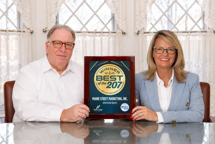 Brenda Lawler & Paul Landry holding a framed “Best of 207” award plaque at a table