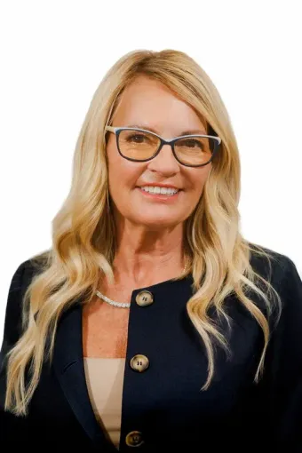 A woman wearing glasses and a black jacket is smiling for the camera.