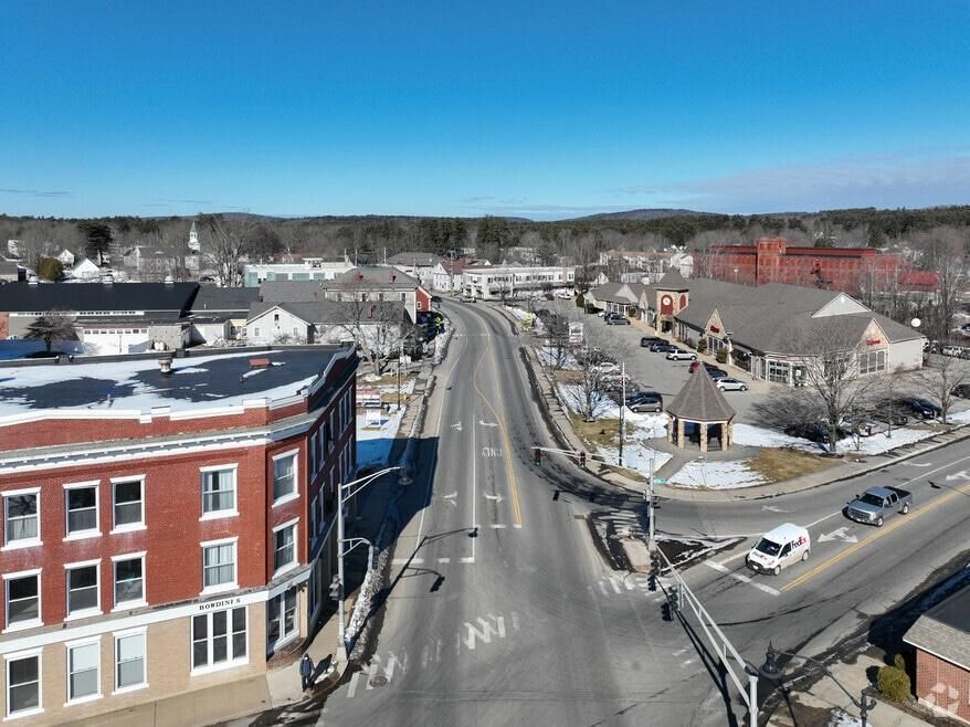 Aerial view of a small town main street with brick buildings, parked cars, and a clear blue sky.