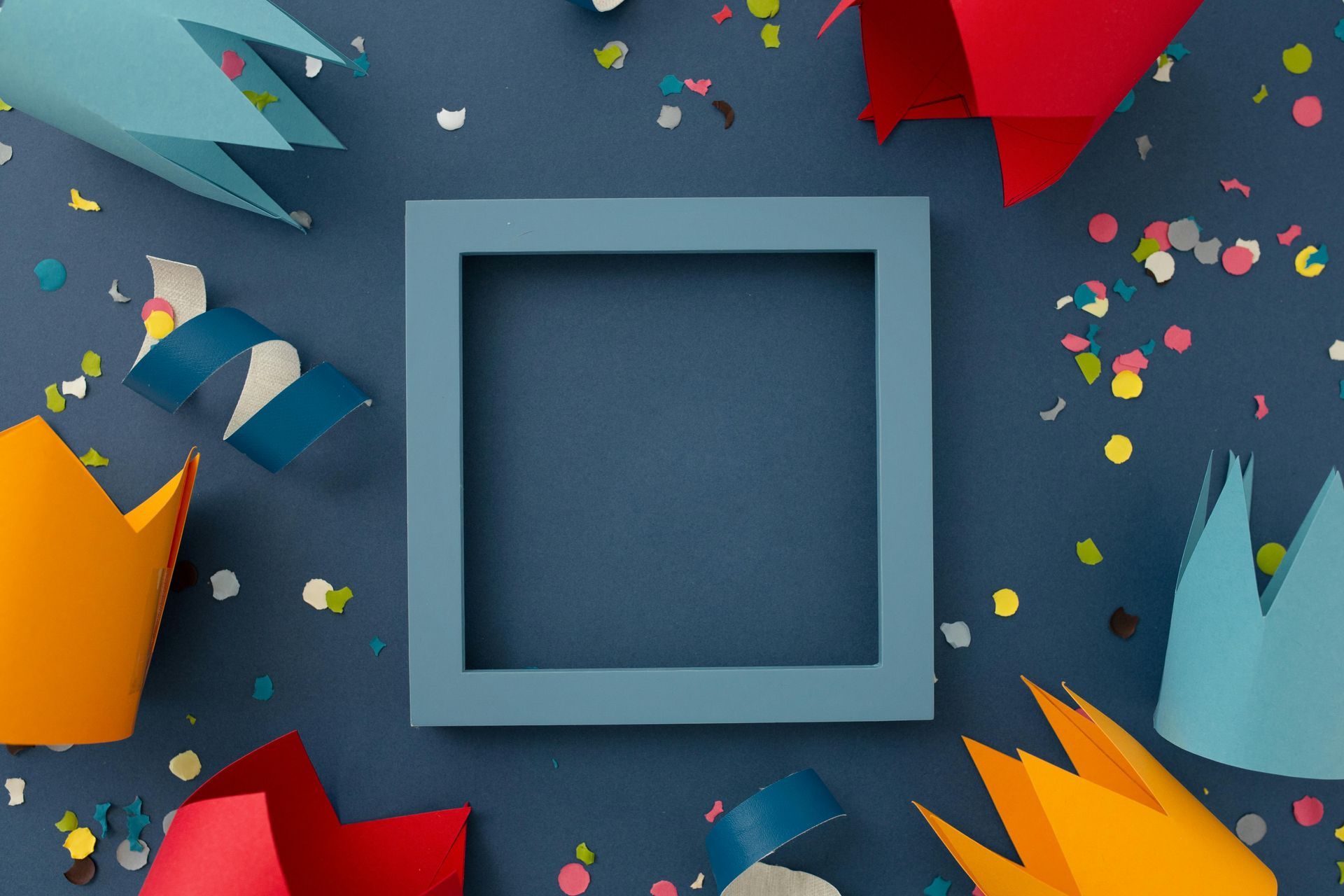 A blue frame is surrounded by paper crowns and confetti on a blue background.
