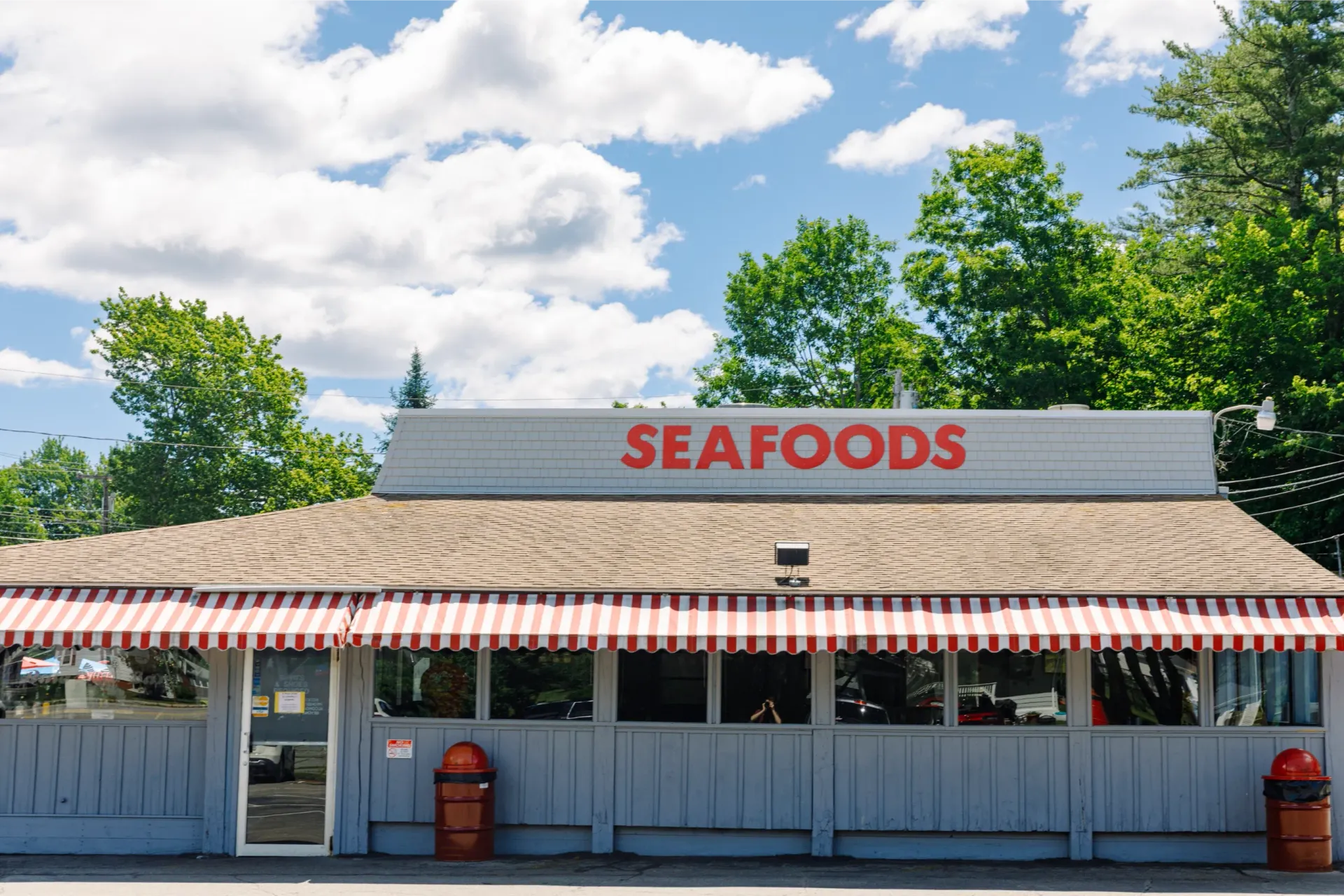 Seafood restaurant storefront with red-and-white awning under a blue sky with clouds