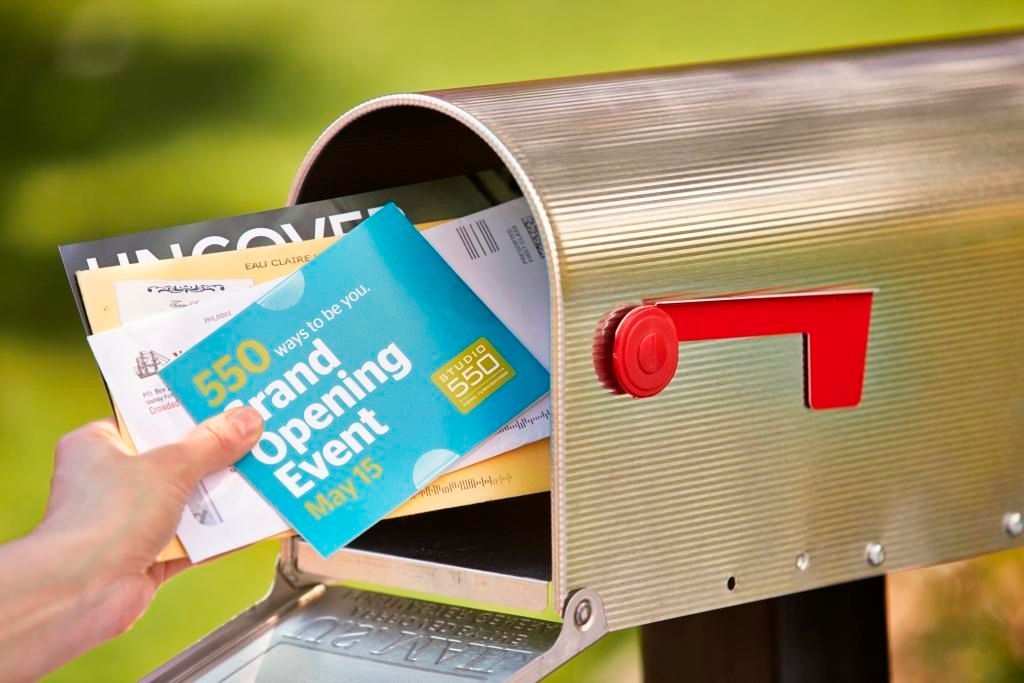 A person is putting a flyer in a mailbox for a grand opening event.