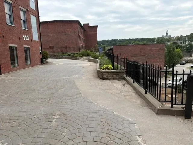 Cobblestone walkway beside red brick buildings and a black iron railing overlooking a valley