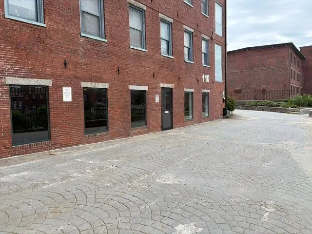 Brick courtyard beside a red-brick building with dark windows and a paved walkway
