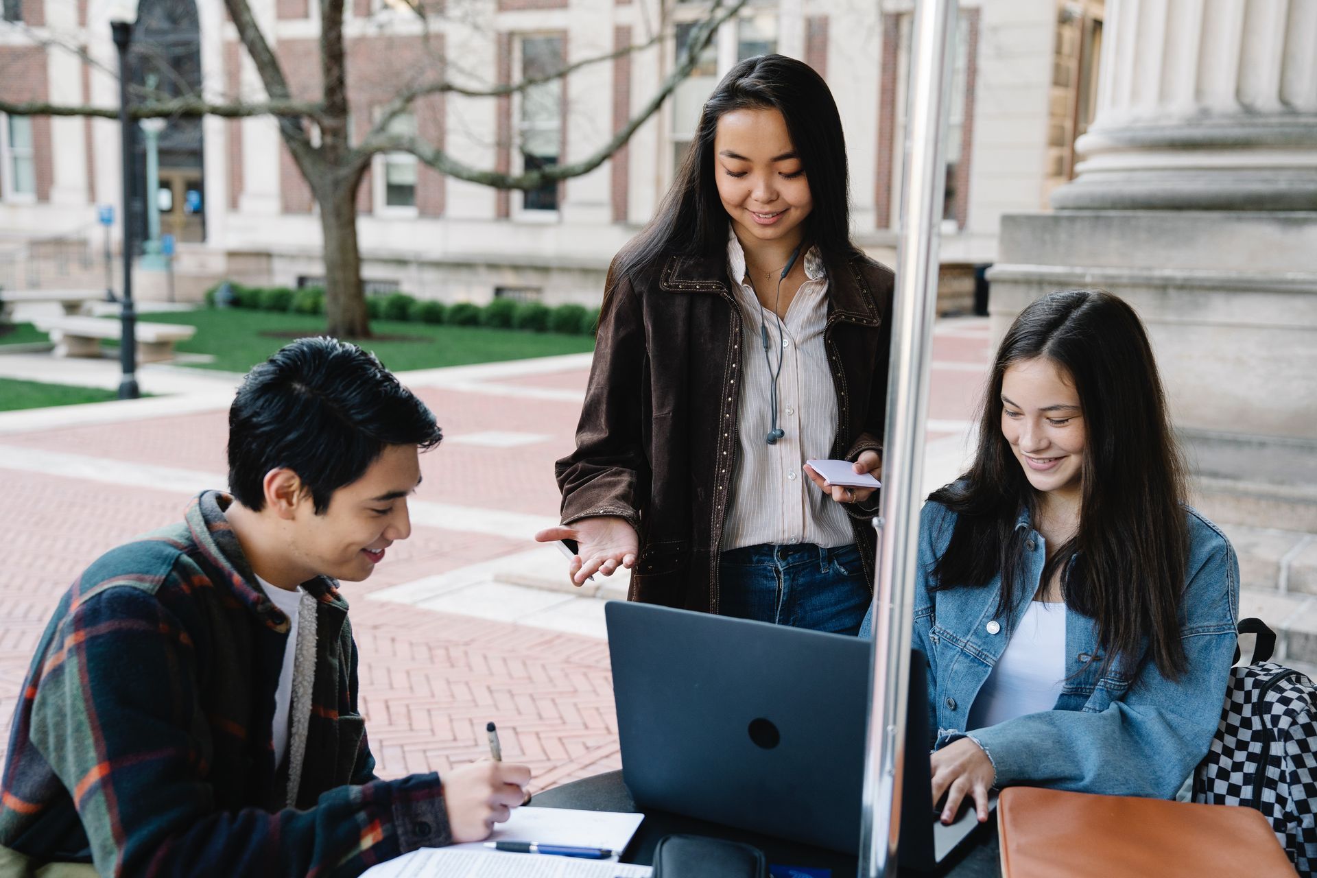 A group of young people are standing around a laptop computer.