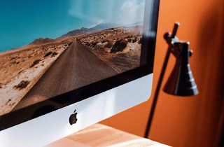 An apple computer is sitting on a wooden desk next to a lamp.
