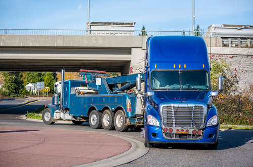 Blue semi-truck with flatbed trailer driving under an overpass on a roadway