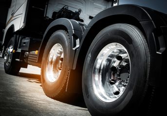 Close-up of a black truck’s chrome wheels on a road, with bright sunlight reflecting off the rims