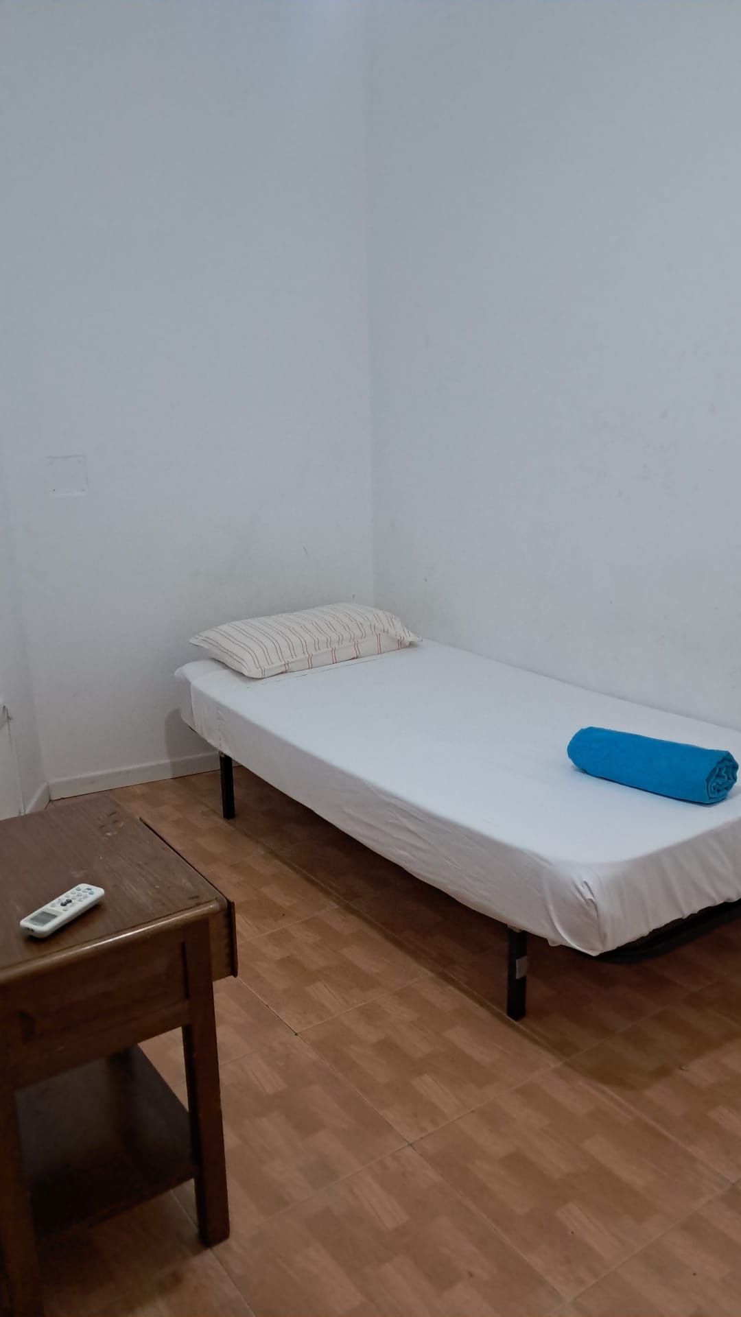 Un dormitorio pequeño y escasamente amueblado con una cama individual, una mesita de noche y una toalla azul.