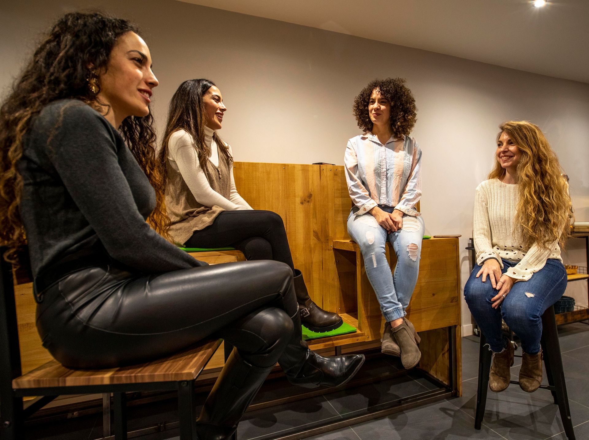 Cuatro mujeres sentadas y hablando en asientos de madera en el interior.