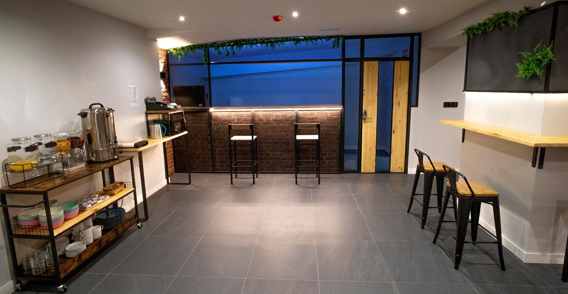 Vista interior de una cafetería moderna con barra, taburetes y mostrador de servicio con estación de café.