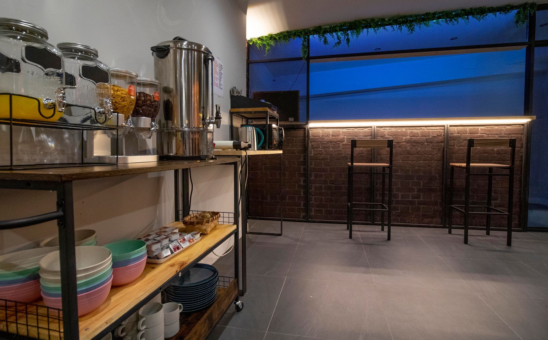 Área de desayuno buffet con dispensadores de comida, estanterías y asientos de bar.