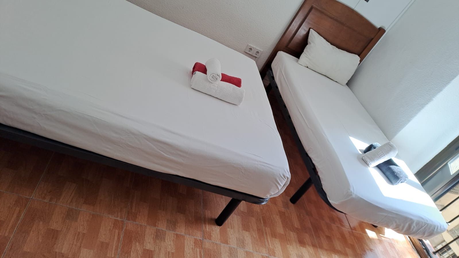 Dos camas individuales con sábanas blancas en una habitación con suelo de madera.