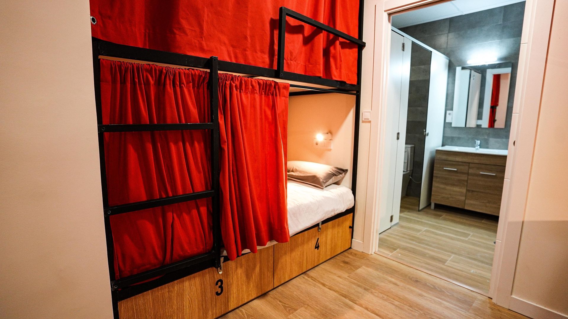 Una litera con cortinas rojas está en una habitación al lado de un baño.