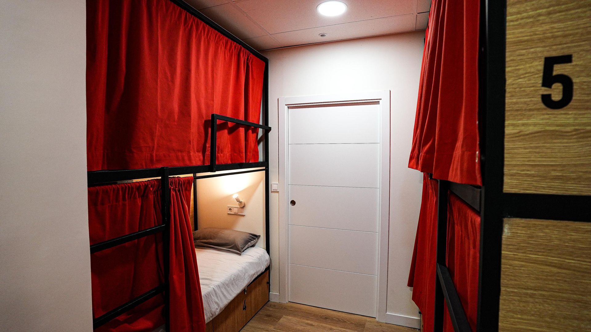 Una litera con cortinas rojas y el número 5 en la pared.