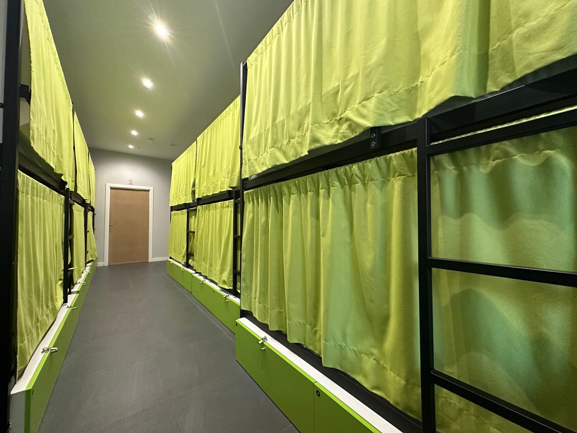 Literas en un pasillo con cortinas de color amarillo brillante, suelo gris y una puerta al final.
