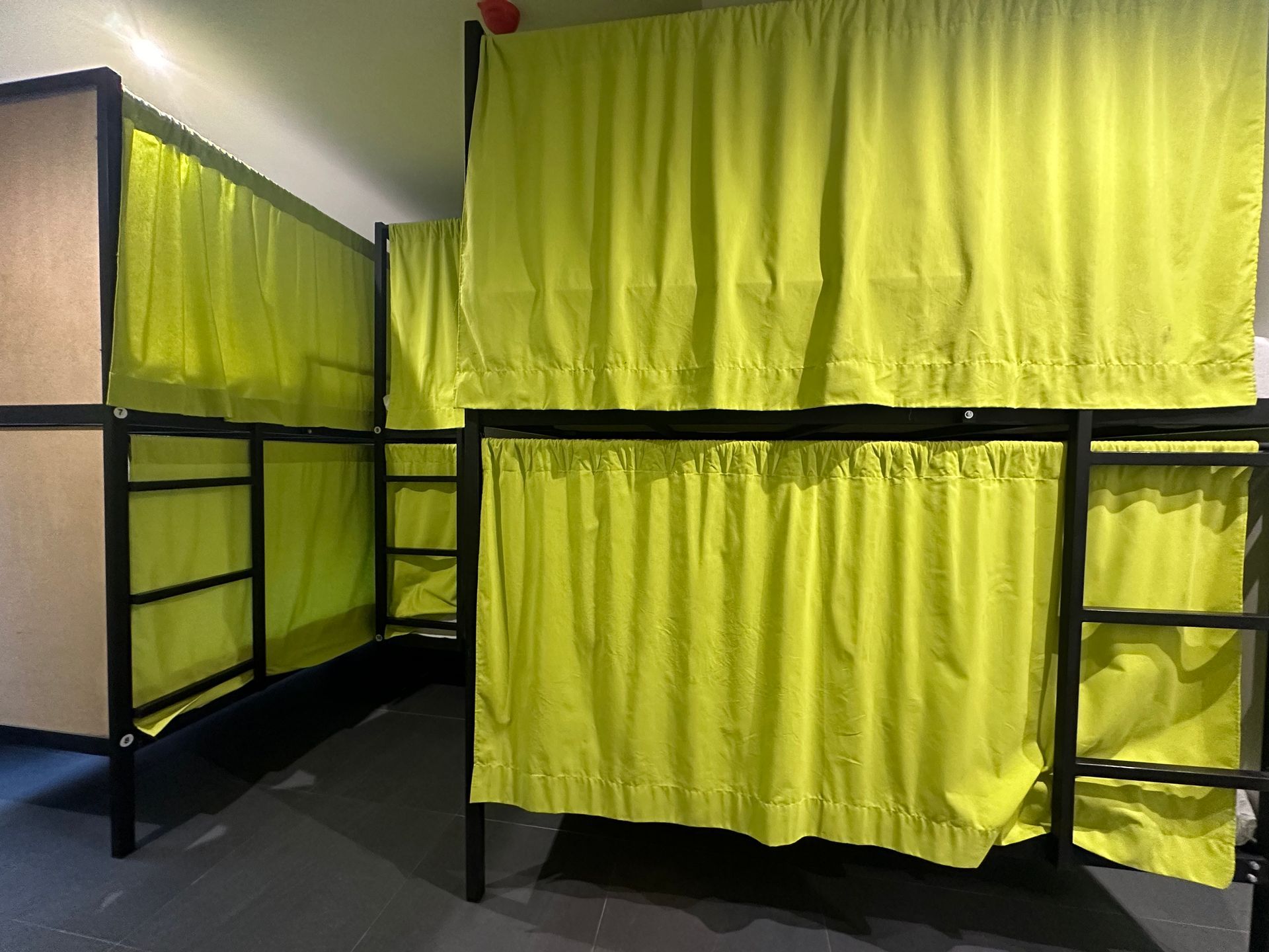 Literas con marcos negros y cortinas de privacidad de color amarillo brillante en una habitación.