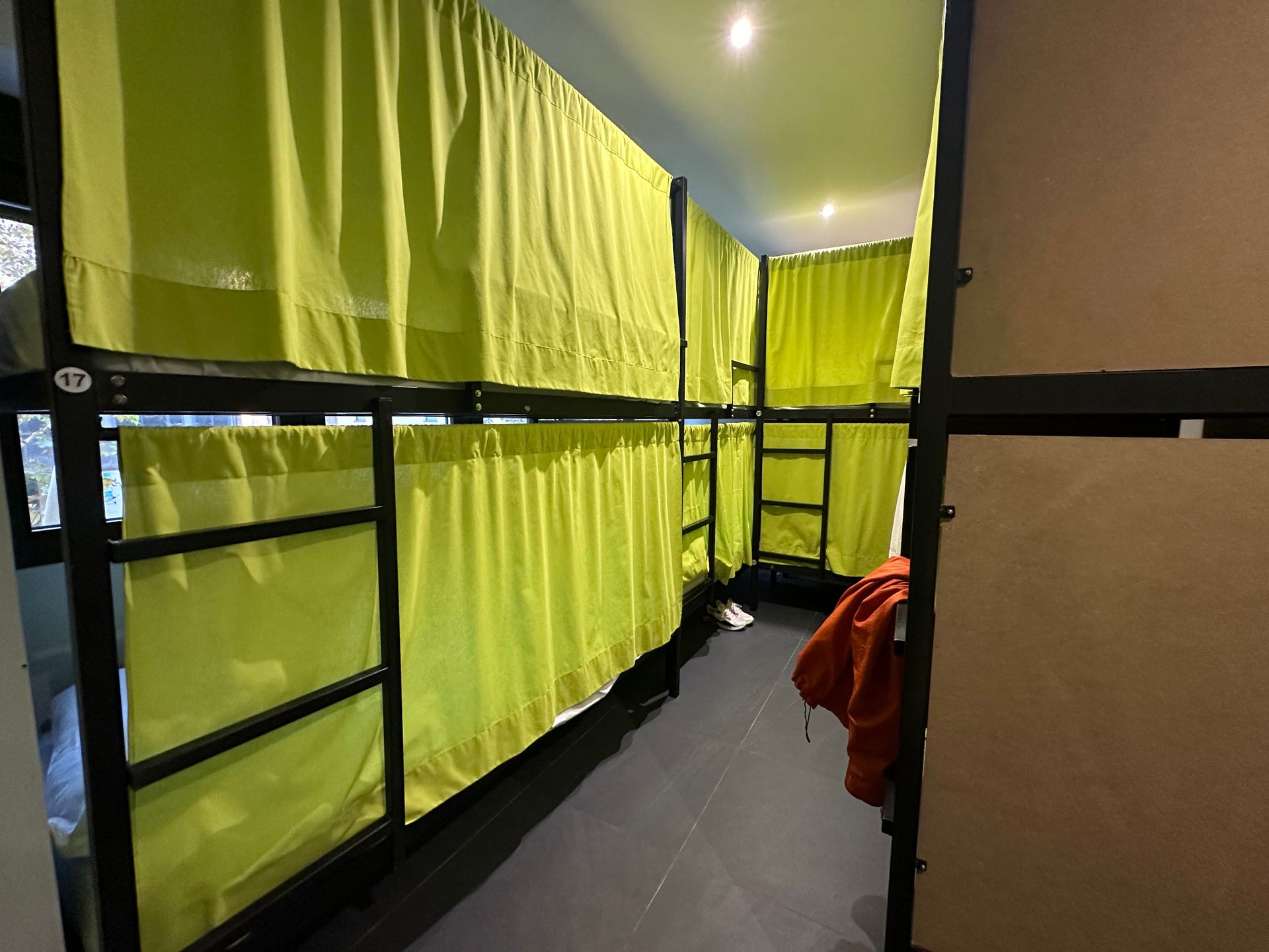 Literas en una habitación de albergue, cada una con cortinas verdes para mayor privacidad, marcos de metal oscuro.