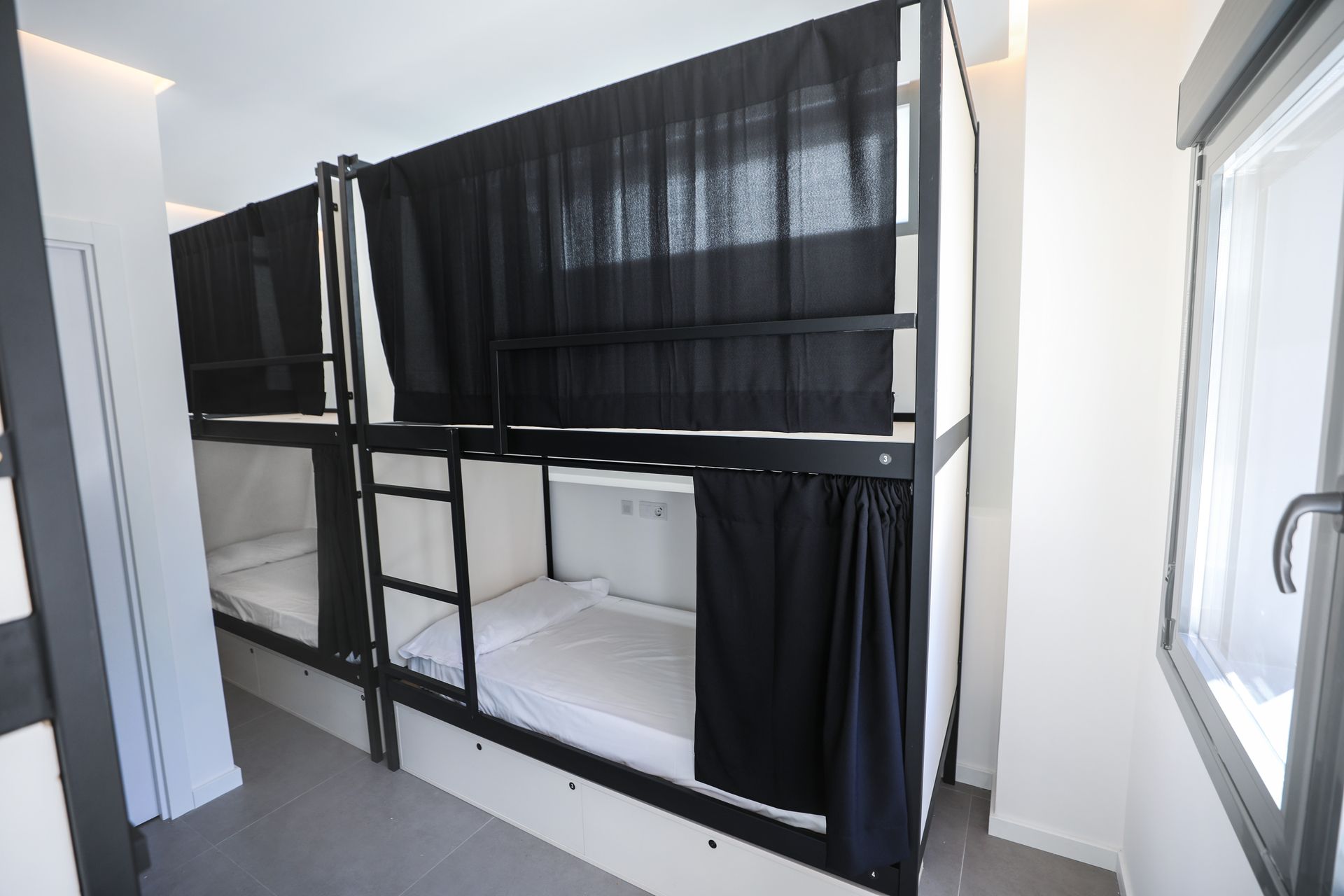 Una litera con cortinas negras está en una habitación al lado de una ventana.