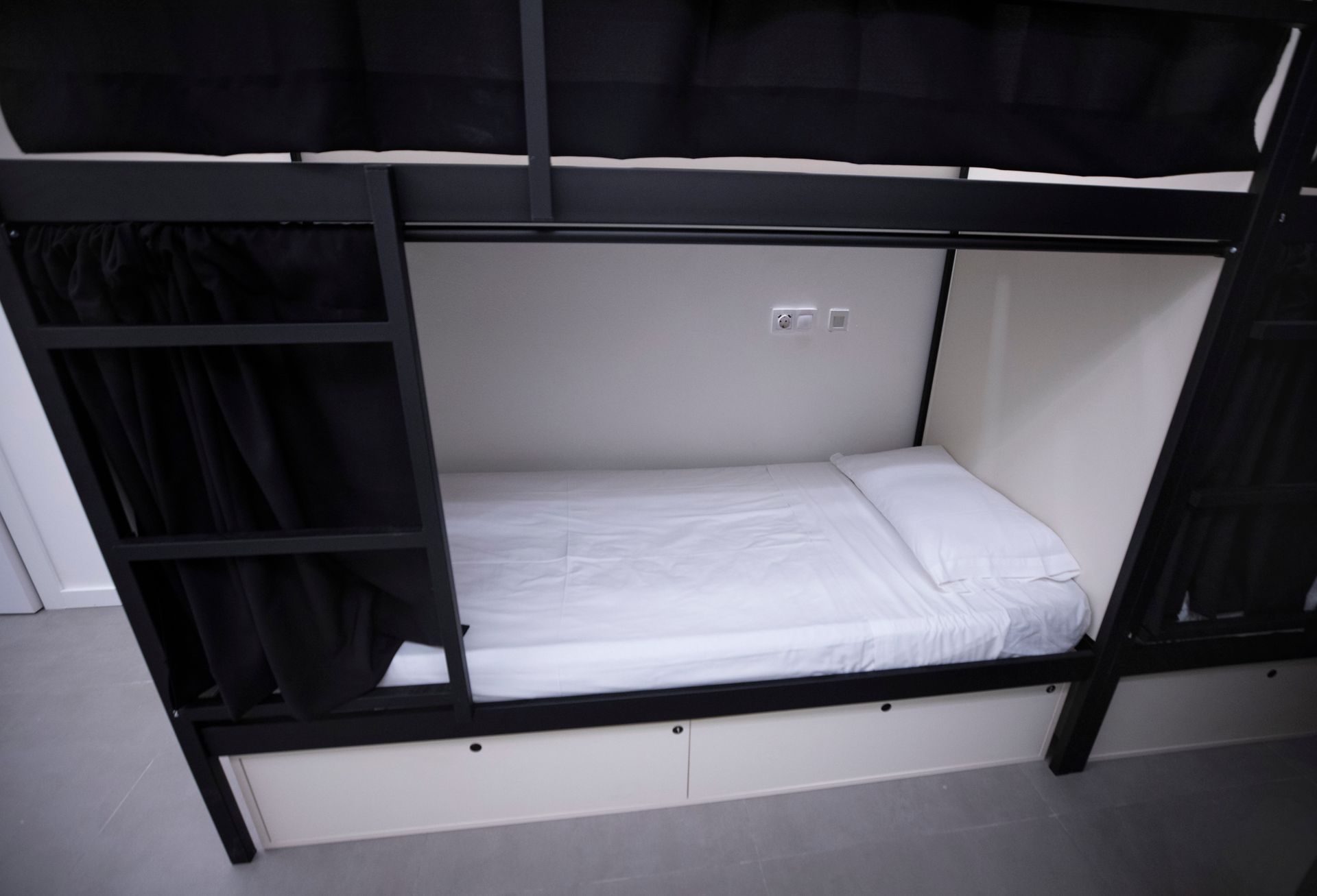 Una litera con sábanas blancas y cortinas negras