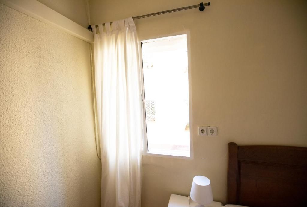 Un dormitorio con una cama y una ventana con cortinas blancas.