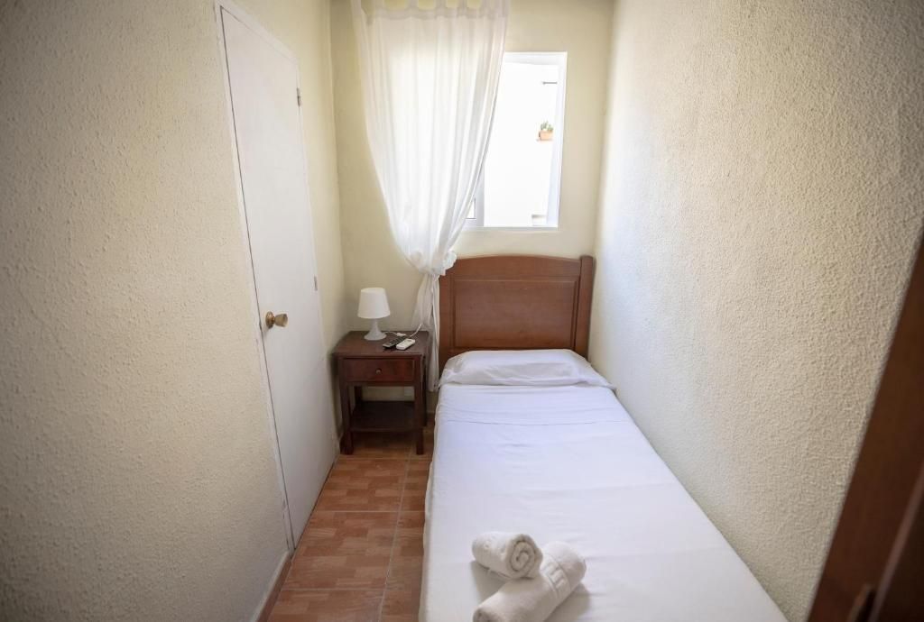 Un dormitorio pequeño con una cama individual, mesita de noche, lámpara y ventana.