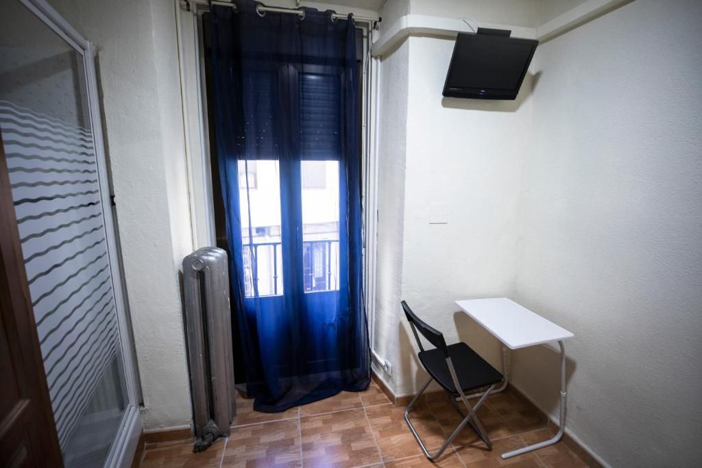 Una pequeña habitación con una mesa y una silla y un televisor en la pared.