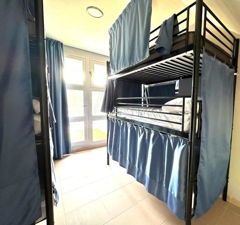Una litera con cortinas azules está en una habitación con ventana.