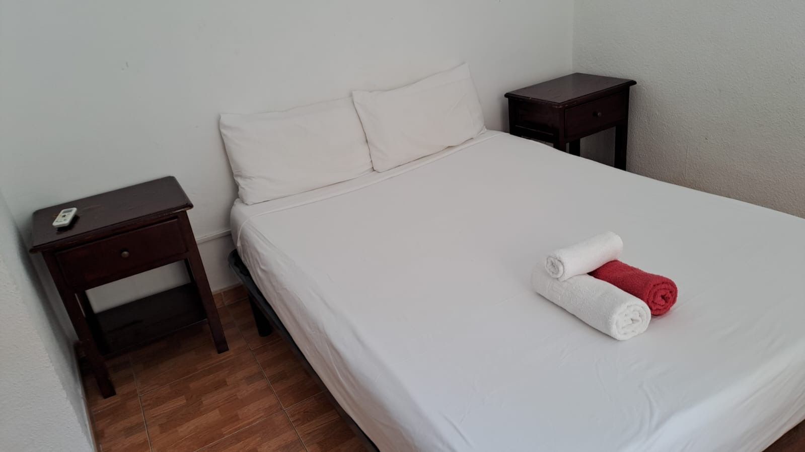 Dormitorio con sábanas blancas, dos toallas enrolladas y dos mesitas de noche.