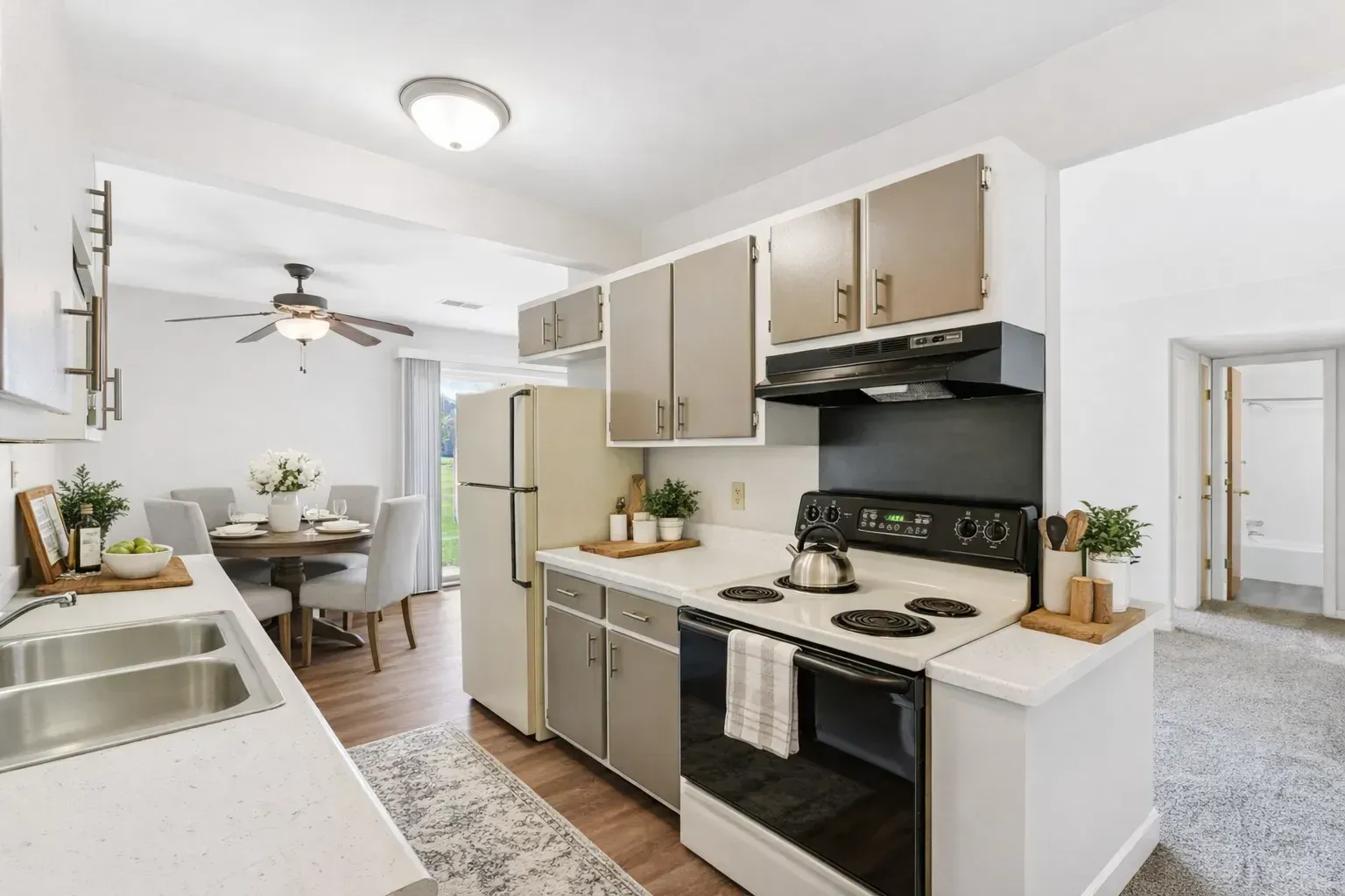 A kitchen with beige cabinets, a stainless steel stove, and a refrigerator next to a dining area with a table and chairs.