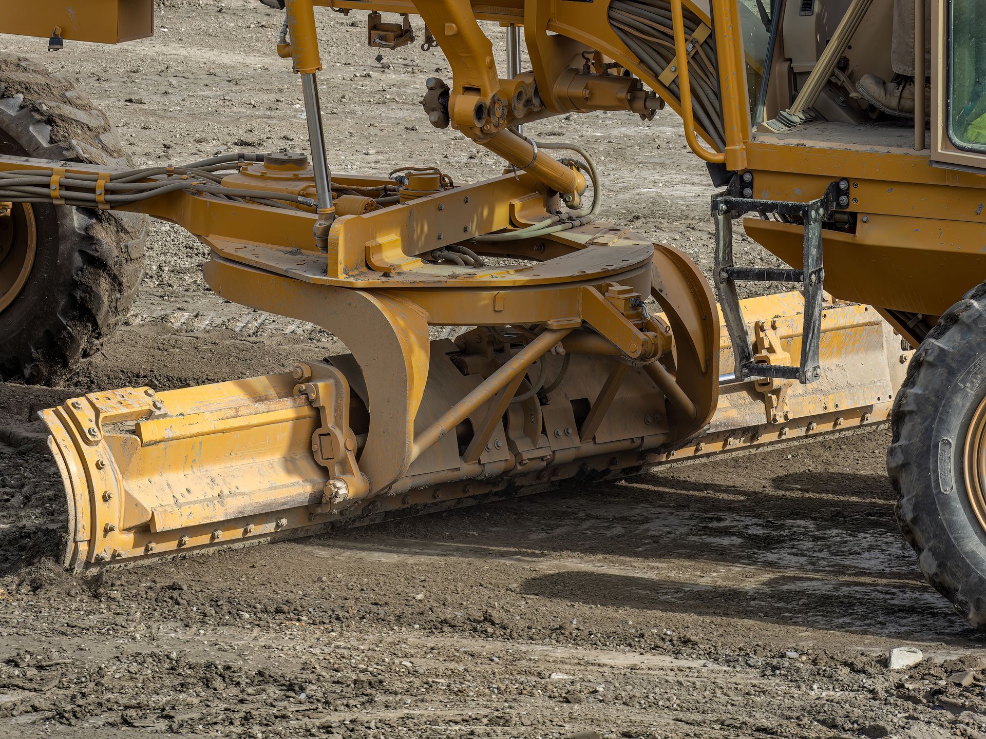 Yellow road grader smoothing dirt surface.