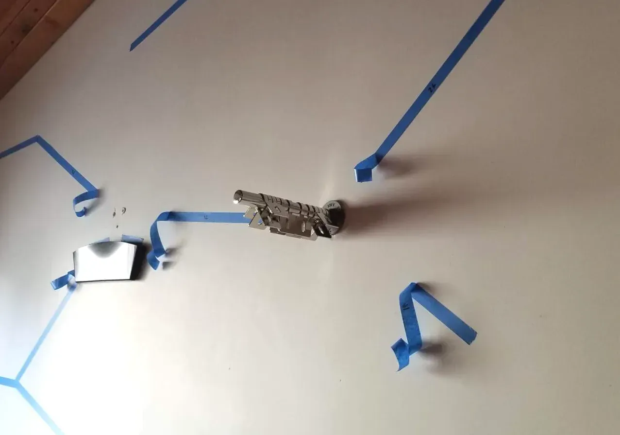 Close-up of a stainless steel Catscapes central bracket mounted on a wall with blue painter's tape marking installation points.
