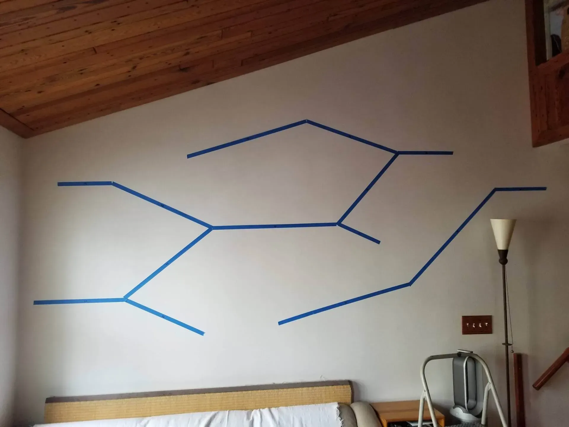 Blue painter's tape on a wall outlining a geometric cat shelf design.