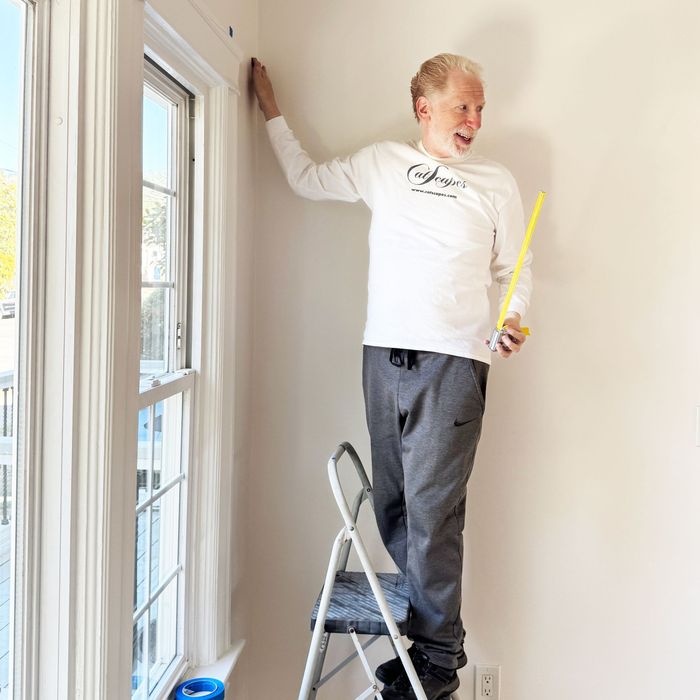 Aaron Feldman in a Catscapes long-sleeve shirt holding a yellow measuring tape for cat wall shelf placement.