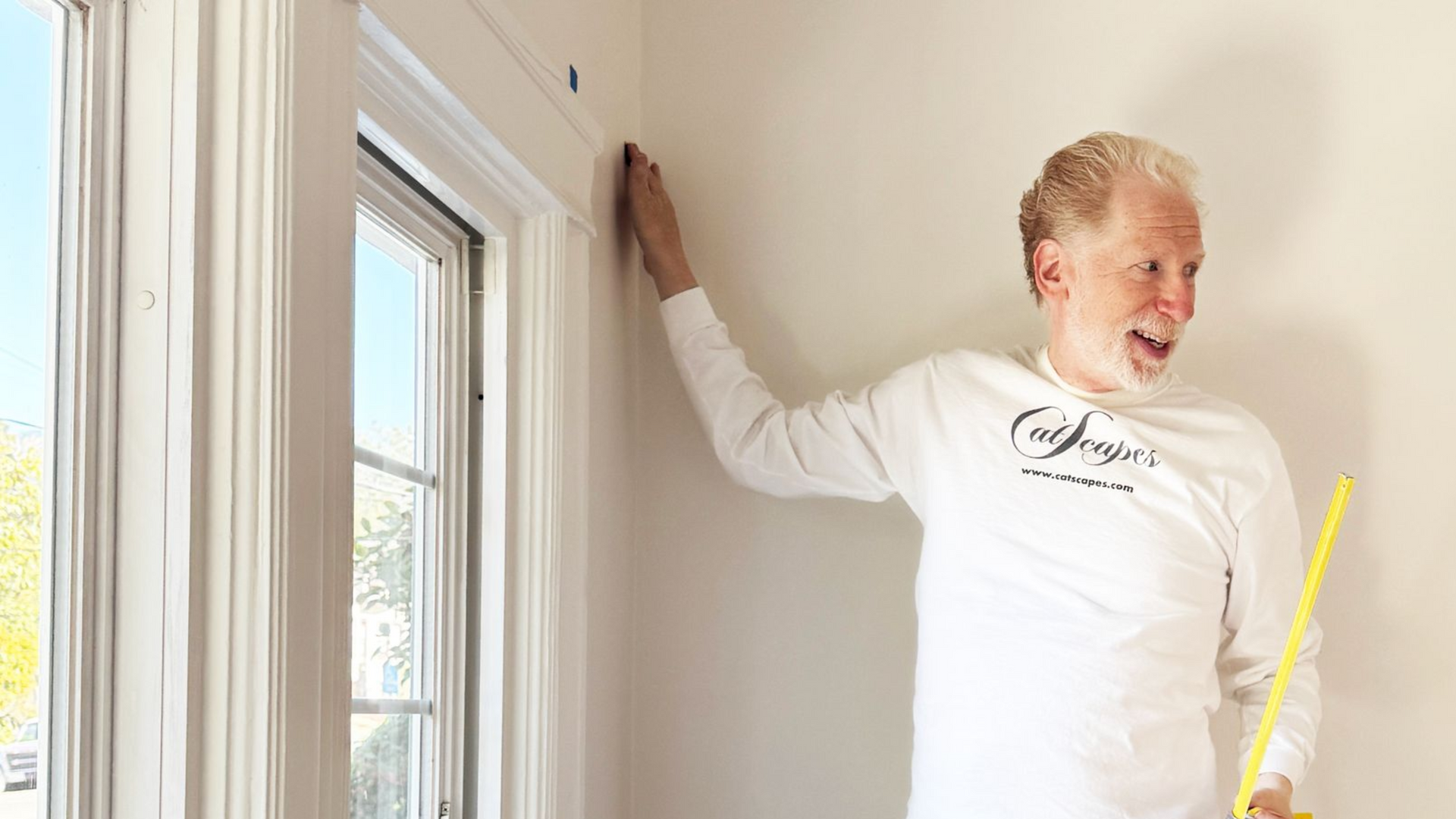 Aaron Feldman in a Catscapes long-sleeve shirt holding a yellow measuring tape for cat wall shelf placement.